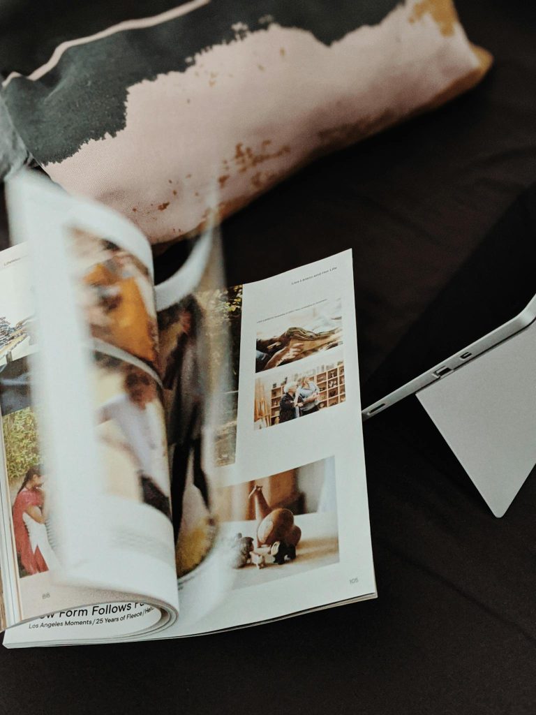 Close-up of an open magazine with blurred pages and a tablet on a dark surface.
